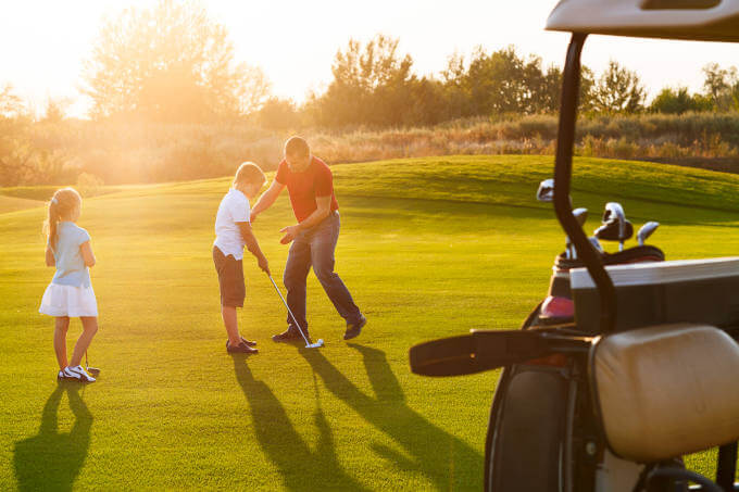 Kids at a golf field holding golf clubs studying with trainer - Depositphotos-86398860-xl-2015.jpg