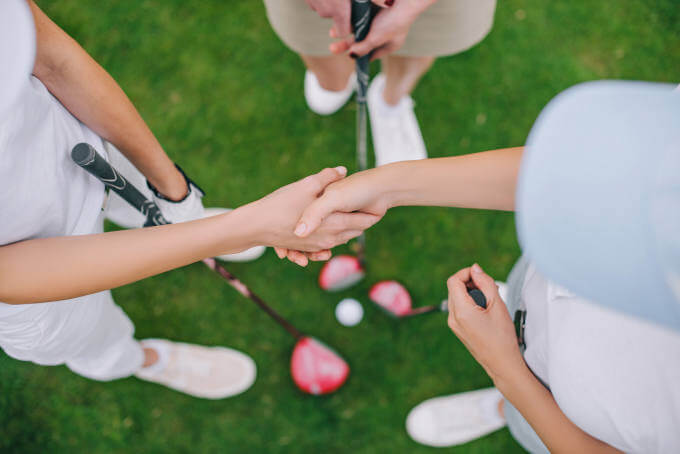 Overhead view of female golf players with golf clubs shaking hands while standing on green lawn - Depositphotos_204322264_xl-2015